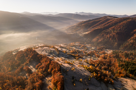 Aerial view of the autumn landscape featuring colorful forests rolling hills covered in frost and morning fog in the valley in Kvasy Zakarpattia Oblast Ukraine. Aerial view of the autumn landscape featuring colorful forests rolling hills covered in frost and morning fog in the valley in Kvasy Zakarpattia Oblast Ukraine.