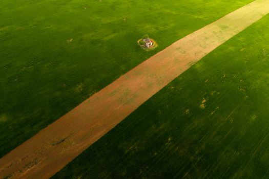 Aerial view of a small isolated structure nestled in a vibrant green agricultural field with a diagonal dirt path cutting through the landscape in Cejkovice South Moravian Region Czechia.