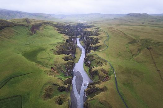 Aerial view of Fjadrargljufur canyon with a winding river flowing between steep moss covered cliffs under a cloudy sky in Skaftarhreppur Iceland. Aerial view of Fjadrargljufur canyon with a winding river flowing between steep moss covered cliffs under a cloudy sky in Skaftarhreppur Iceland.