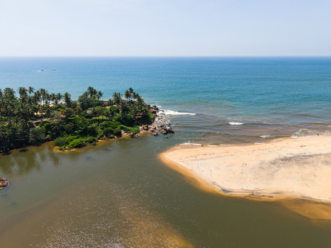 Aerial view of a tropical coastline where a river meets the turquoise ocean featuring a sandy beach and lush palm trees under a clear blue sky in Galle Southern Province Sri Lanka.