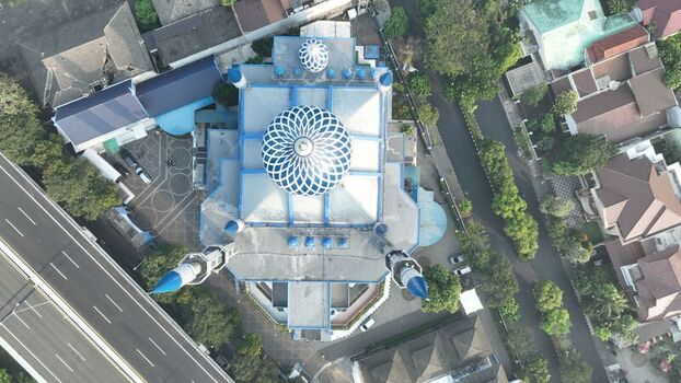 Aerial view of a mosque with a distinctive blue and white dome and minarets surrounded by urban rooftops and a nearby highway in Bekasi Barat West Java Indonesia. Aerial view of a mosque with a distinctive blue and white dome and minarets surrounded by urban rooftops and a nearby highway in Bekasi Barat West Java Indonesia.