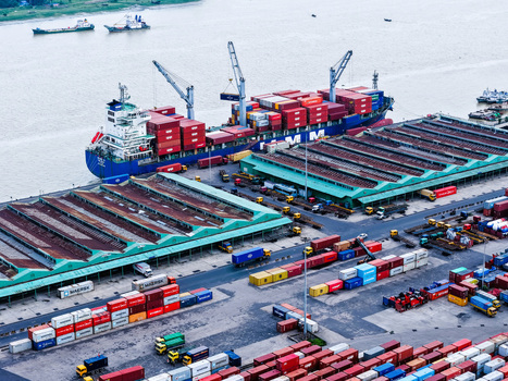 Aerial view of Chattogram Port with a large container ship colorful shipping containers industrial warehouses with green roofs and trucks in Chittagong Chittagong Division Bangladesh.