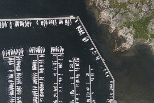 Aerial view of Sando marina with numerous sailboats docked in parallel rows along wooden piers surrounded by rocky coastline and dark water in Vallda Hallands lan Sweden.