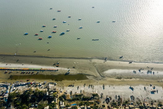 Aerial view of Kuakata beach with fishing boats in the Bay of Bengal colorful umbrellas along the sandy shore and coastal structures in Kuakata Barisal Division Bangladesh. Aerial view of Kuakata beach with fishing boats in the Bay of Bengal colorful umbrellas along the sandy shore and coastal structures in Kuakata Barisal Division Bangladesh.