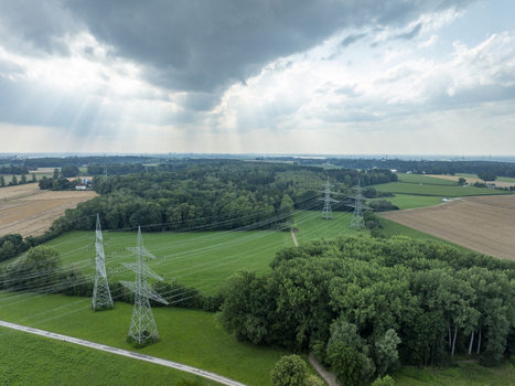 Aerial view of Umspannwerk Ottenhofen featuring high voltage power transmission towers and lines across green fields and forest under a dramatic sky in Ottenhofen Bayern Germany.