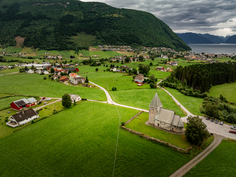 Aerial view of Hove Church surrounded by lush green fields traditional houses and rolling hills under a cloudy sky in Vik i Sogn Vestland Norway. Aerial view of Hove Church surrounded by lush green fields traditional houses and rolling hills under a cloudy sky in Vik i Sogn Vestland Norway.