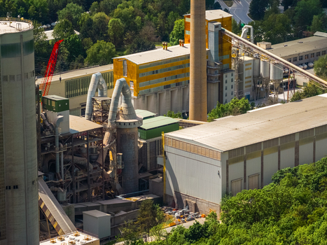Aerial view of the industrial cement plant with tall chimneys silos and conveyor belts surrounded by lush green forest in Mokra Horakov Jihomoravsky kraj Czechia. Aerial view of the industrial cement plant with tall chimneys silos and conveyor belts surrounded by lush green forest in Mokra Horakov Jihomoravsky kraj Czechia.