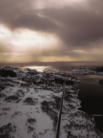 Aerial view of snow blanketed isles and a narrow road stretching towards the horizon under a dramatic cloudy sky Svolv&aelig;r Nordland Norway.