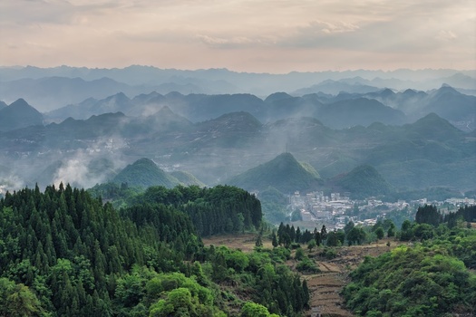 Aerial view of misty karst mountains and a traditional village nestled among lush green forests under a soft overcast sky Gaoxing Miao Village Guizhou China. Aerial view of misty karst mountains and a traditional village nestled among lush green forests under a soft overcast sky Gaoxing Miao Village Guizhou China.