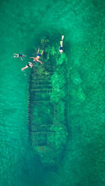 Aerial view of the Kontesa shipwreck submerged in crystal clear turquoise water with snorkelers swimming above the hull in Necujam Split Dalmatia County Croatia. Aerial view of the Kontesa shipwreck submerged in crystal clear turquoise water with snorkelers swimming above the hull in Necujam Split Dalmatia County Croatia.