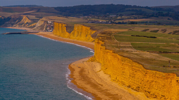 Aerial view of the golden sandstone cliffs of West Bay along the Jurassic Coast with a sandy beach and rolling green hills in West Bay England United Kingdom. Aerial view of the golden sandstone cliffs of West Bay along the Jurassic Coast with a sandy beach and rolling green hills in West Bay England United Kingdom.