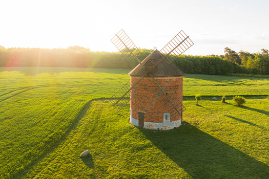 Aerial view of the historic brick windmill surrounded by lush green fields and forest at golden hour sunset Chvalkovice Hradec Kralove Region Czechia.