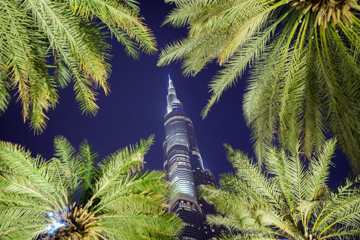 Dubai United Arab Emirates 19 April 2023 View of the illuminated Burj Khalifa skyscraper framed by lush palm tree fronds against a dark night sky. Dubai United Arab Emirates 19 April 2023 View of the illuminated Burj Khalifa skyscraper framed by lush palm tree fronds against a dark night sky.