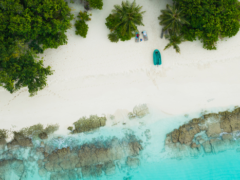 Aerial view of a turquoise boat resting on pristine white sands near lush green trees creating a tropical paradise Vashafaru Island Maldives. Aerial view of a turquoise boat resting on pristine white sands near lush green trees creating a tropical paradise Vashafaru Island Maldives.