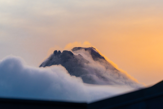 View of the Arenal Volcano peak partially shrouded in thick clouds during a golden sunset in Costa Rica.