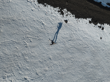 Aerial view of a person walking on the snow covered south slope of Mount Etna with a long shadow and dark volcanic soil in Nicolosi Sicilia Italy. Aerial view of a person walking on the snow covered south slope of Mount Etna with a long shadow and dark volcanic soil in Nicolosi Sicilia Italy.