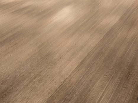 Aerial view of a freshly plowed agricultural field with distinct furrows and soil patterns in Poland.