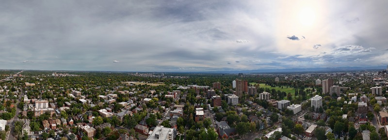 Aerial view of the Denver cityscape featuring residential neighborhoods lush green trees high rise buildings and distant mountains under a cloudy sky in Denver Colorado United States. Aerial view of the Denver cityscape featuring residential neighborhoods lush green trees high rise buildings and distant mountains under a cloudy sky in Denver Colorado United States.