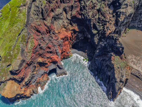 Aerial view of rugged cliffs meet the turquoise sea a striking contrast of red rock and blue water at Capelinhos Volcano Capelo A&ccedil;ores Portugal.