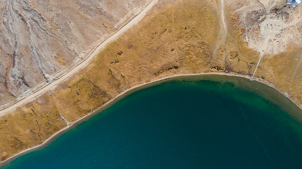 Aerial view of Shausar Lake with its deep blue waters and a dirt road winding along the dry grassy shoreline in Skardu Gilgit Pakistan.