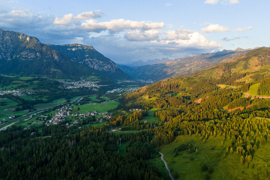 Aerial view of Fiemme Valley with lush green forests rolling hills and small mountain villages under a soft golden hour light Trentino Alto Adige Italy.