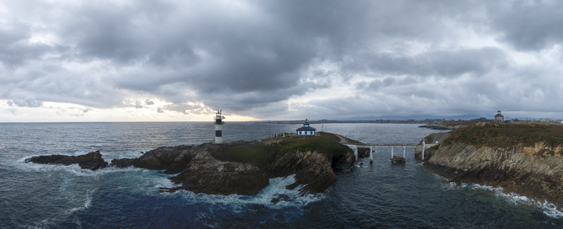 Aerial view of the Illa Pancha lighthouse on a rocky islet connected by a bridge to the mainland surrounded by the Atlantic Ocean under a cloudy sky in Ribadeo Galicia Spain.