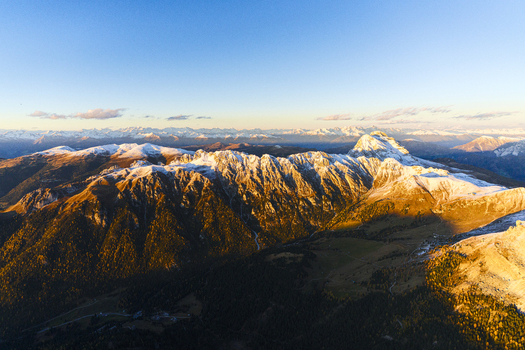 Aerial view of the golden light kisses the snow dusted Puez Odle range peaks casting long shadows across the valleys a serene alpine landscape unfolds Trentino South Tyrol Italy.
