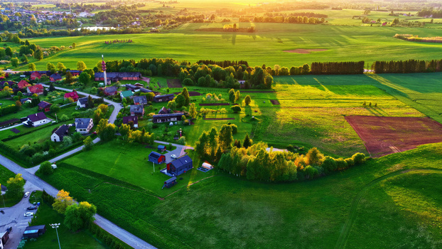 Aerial view of a rural village with scattered houses lush green fields and trees bathed in the warm light of the golden hour in Latvija. Aerial view of a rural village with scattered houses lush green fields and trees bathed in the warm light of the golden hour in Latvija.