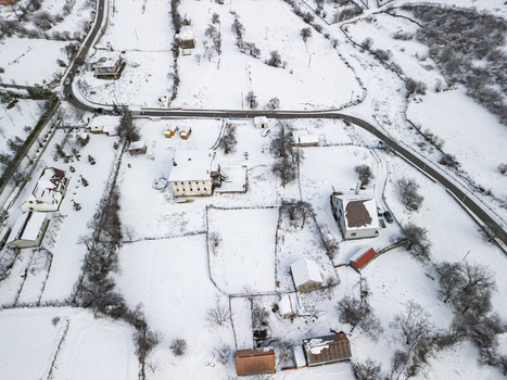 Aerial view of houses and rural buildings surrounded by snow covered fields and a winding road in the mountainous landscape of Boge Shkoder County Albania. Aerial view of houses and rural buildings surrounded by snow covered fields and a winding road in the mountainous landscape of Boge Shkoder County Albania.