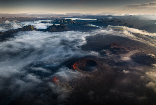 Aerial view of volcanic craters and rugged highlands partially covered by flowing mist under a dramatic sky Iceland.