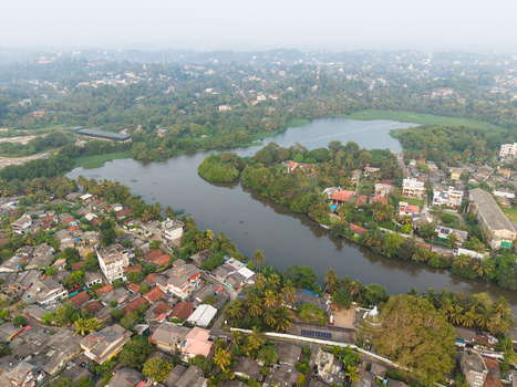Aerial view of the winding river surrounded by dense tropical greenery and urban rooftops under a hazy sky in Galle Southern Province Sri Lanka.
