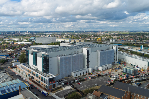 Aerial view of a large modern data center facility with industrial cooling units on the roof surrounded by urban infrastructure and roads in the United Kingdom. Aerial view of a large modern data center facility with industrial cooling units on the roof surrounded by urban infrastructure and roads in the United Kingdom.