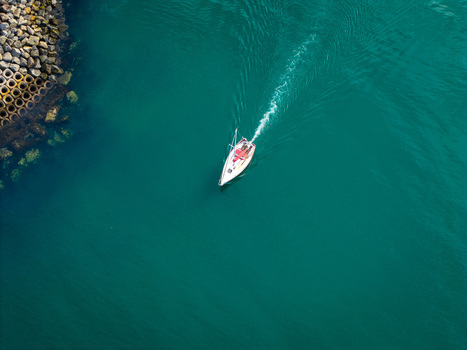 Aerial view of a sailboat leaving a wake in the turquoise waters of Bangor Harbour with a stone breakwater visible in the corner in Bangor Northern Ireland United Kingdom.