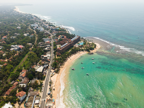 Aerial view of the tropical coastline featuring turquoise waters sandy beaches with people and coastal resorts in Hikkaduwa Southern Province Sri Lanka. Aerial view of the tropical coastline featuring turquoise waters sandy beaches with people and coastal resorts in Hikkaduwa Southern Province Sri Lanka.