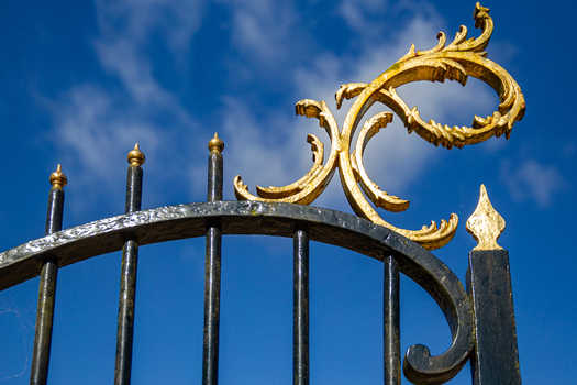 View of the ornate gilded scrollwork on the black wrought iron gate of Castle Groeneveld under a bright blue sky in Baarn Utrecht Netherlands.