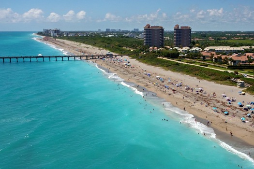 Aerial view of Juno Beach Pier stretching into the turquoise Atlantic Ocean with people on the sandy shore and coastal buildings Juno Beach Florida United States. Aerial view of Juno Beach Pier stretching into the turquoise Atlantic Ocean with people on the sandy shore and coastal buildings Juno Beach Florida United States.