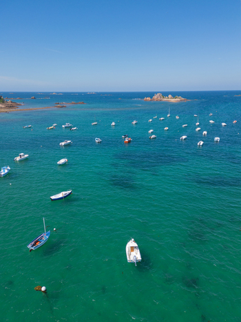Aerial view of Plage de Port Blanc with numerous boats anchored in turquoise waters near rocky islands under a clear blue sky Penvenan Bretagne France. Aerial view of Plage de Port Blanc with numerous boats anchored in turquoise waters near rocky islands under a clear blue sky Penvenan Bretagne France.