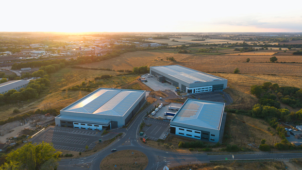 Aerial view of modern industrial warehouses surrounded by fields under the warm glow of sunset in Wellingborough England United Kingdom. Aerial view of modern industrial warehouses surrounded by fields under the warm glow of sunset in Wellingborough England United Kingdom.