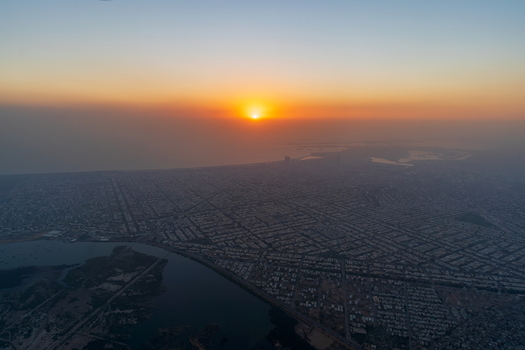 Aerial view of the sprawling urban landscape of Karachi at sunset with dense residential grids coastal waters and a hazy golden horizon in Karachi Sindh Pakistan.