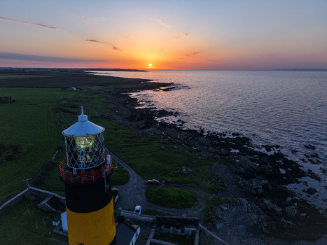 Aerial view of St. John s Point Lighthouse illuminated at sunset with rocky coastline and calm sea in Newcastle Northern Ireland United Kingdom. Aerial view of St. John s Point Lighthouse illuminated at sunset with rocky coastline and calm sea in Newcastle Northern Ireland United Kingdom.