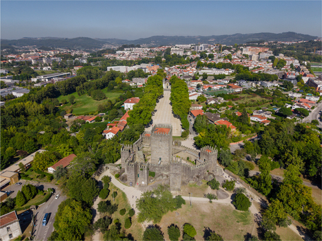 Aerial view of the historic Guimaraes Castle and the nearby Igreja de Sao Miguel do Castelo surrounded by lush green trees and the urban landscape of Guimaraes Braga Portugal. Aerial view of the historic Guimaraes Castle and the nearby Igreja de Sao Miguel do Castelo surrounded by lush green trees and the urban landscape of Guimaraes Braga Portugal.