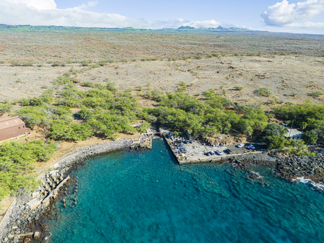Aerial view of Mahukona Beach Park featuring the clear turquoise waters of the bay a stone pier with parked vehicles and the surrounding arid landscape in Waimea Hawaii United States.