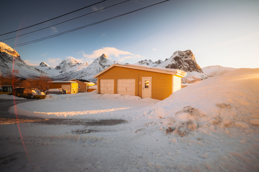 View of the golden light bathing a yellow garage and a snow covered landscape under the watchful gaze of snow capped mountains Indregård Troms Norway. View of the golden light bathing a yellow garage and a snow covered landscape under the watchful gaze of snow capped mountains Indregård Troms Norway.