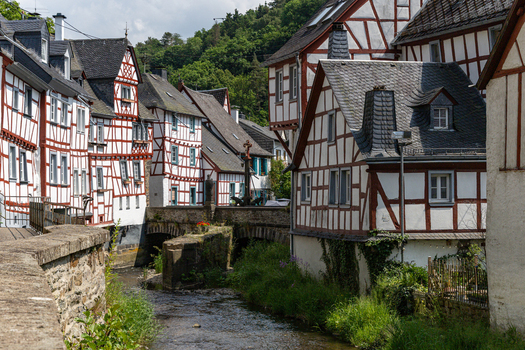 View of traditional half timbered houses along the Elzbach river with a stone bridge and lush green hills in Monreal Rhineland Palatinate Germany. View of traditional half timbered houses along the Elzbach river with a stone bridge and lush green hills in Monreal Rhineland Palatinate Germany.