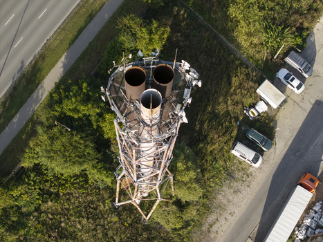 Aerial view of a metal telecommunications tower with three large cylindrical vents at the top surrounded by green trees a road and parked vehicles in Krakow Lesser Poland Voivode Poland.