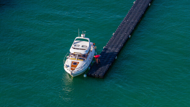 Aerial view of a white motorboat moored to a black floating dock in the turquoise waters of West Bay England United Kingdom. Aerial view of a white motorboat moored to a black floating dock in the turquoise waters of West Bay England United Kingdom.
