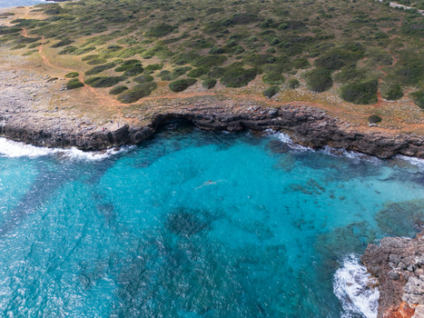 Aerial view of the rugged rocky coastline and crystal clear turquoise waters of a secluded cove with green scrubland and a dirt path Sa Coma Balearic Islands Spain. Aerial view of the rugged rocky coastline and crystal clear turquoise waters of a secluded cove with green scrubland and a dirt path Sa Coma Balearic Islands Spain.