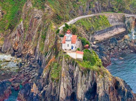 Aerial view of the Faro de Cudillero lighthouse perched on a steep rocky cliff overlooking the blue sea and lush green hills Cudillero Asturias Spain. Aerial view of the Faro de Cudillero lighthouse perched on a steep rocky cliff overlooking the blue sea and lush green hills Cudillero Asturias Spain.