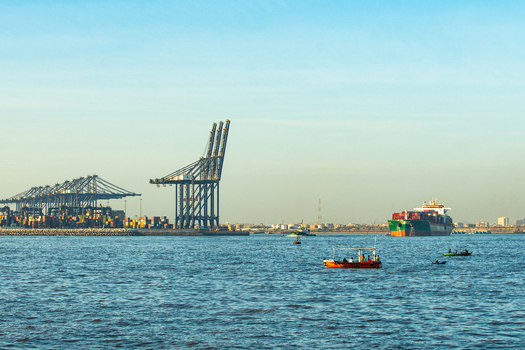 View of the Port of Karachi with large container cranes a cargo ship and small fishing boats on the water in Karachi Sindh Pakistan.