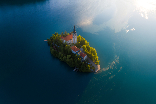 Aerial view of the Pilgrimage Church of the Assumption of Maria on Bled Island surrounded by calm blue water during golden hour in Bled Radovljica Slovenia.
